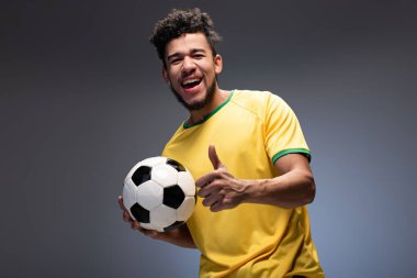 Sarı tişörtlü, gülle tutan ve gri tişörtlü mutlu Afro-Amerikan futbol fanatiği.