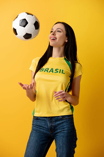 cheerful female football fan throwing up ball on yellow