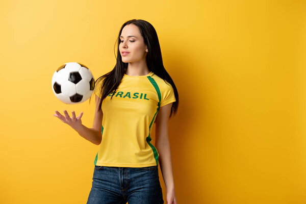 attractive female football fan throwing up ball on yellow