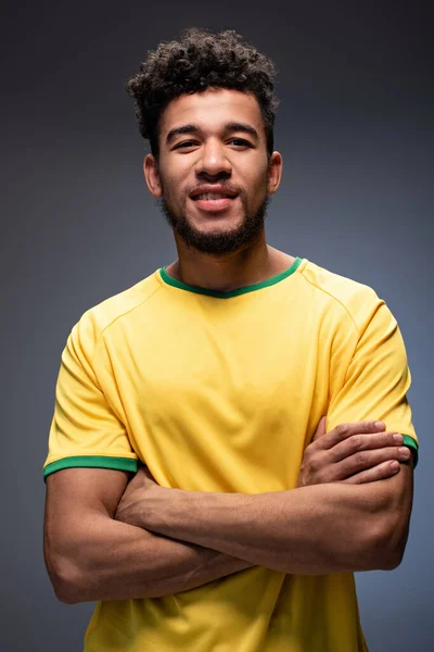 快乐的非洲裔美式足球迷 身穿黄色T恤 双臂交叉 灰色地站在那里 — 图库照片