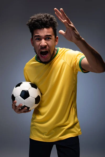 穿着黄色T恤衫的激进的非洲美式足球迷大喊着 拿着灰色的球 — 图库照片