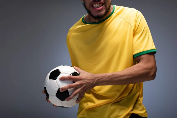 cropped view of emotional football fan in yellow t-shirt holding ball on grey