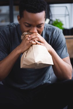 Evde panik atak geçirirken elinde kesekâğıdıyla nefes alan yalnız Afrikalı Amerikalı bir adam.