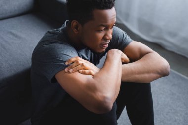 depressed african american man sitting on floor with crossed arms clipart