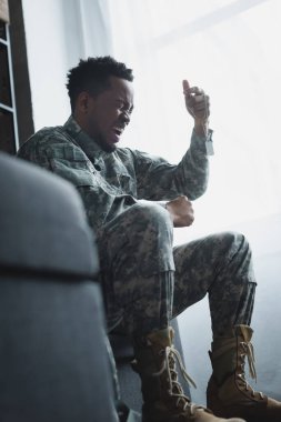 Stresli bir Afro-Amerikan askeri evde asker rozeti taşıyor ve bağırıyor. Travma sonrası stres bozukluğu yaşıyor.