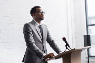 Konferans salonunda mikrofonla podyumda duran kendine güvenen Afro-Amerikan iş konuşmacısı