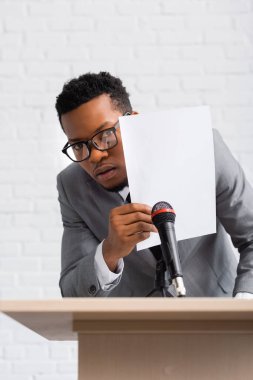 İş konferansı sırasında kağıdın arkasına saklanan korkmuş Afrikalı Amerikalı konuşmacı