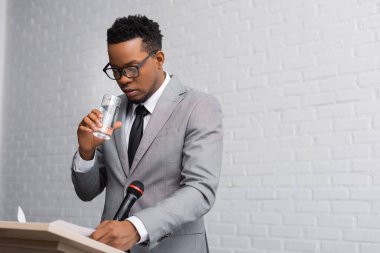 nervous african american businessman drinking water on business conference in office  clipart