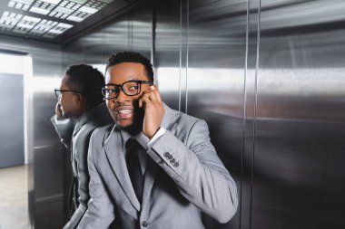 Stresli Afrikalı Amerikalı iş adamı akıllı telefondan konuşuyor ve asansörde panik atak geçiriyor.