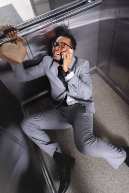 Ağlayan Afro-Amerikan iş adamı. Elinde kese kağıdıyla akıllı telefondan konuşuyor ve asansörde panik atak geçiriyor.