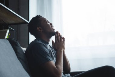 emotional african american man yelling with hands together on sofa at home clipart