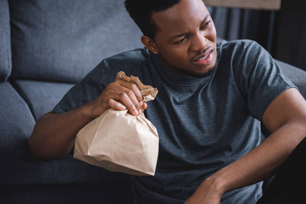 Worried african american man holding paper bag while having panic attack at home
