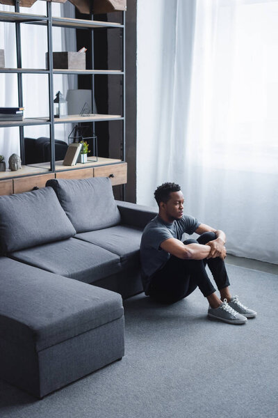 lonely sad african american man sitting on floor at home