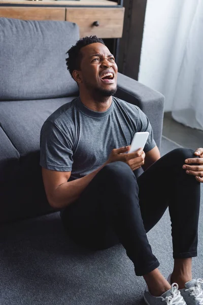 Напряженный Африканский Американец Кричит Использует Смартфон Дома — стоковое фото