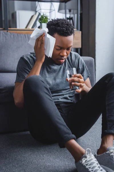 Стресовий Спітнілий Афроамериканський Чоловік Тримає Склянку Води Серветок Вдома — стокове фото