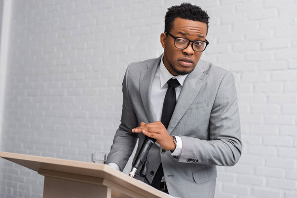 frustrated african american speaker covering microphone during business conference in office
