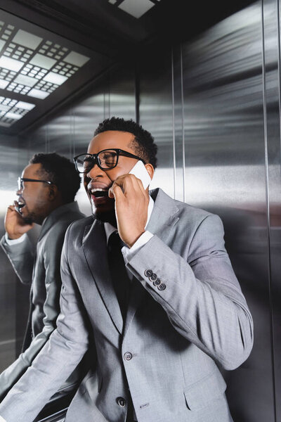 stressed african american businessman crying and talking on smartphone while suffering from panic attack in elevator