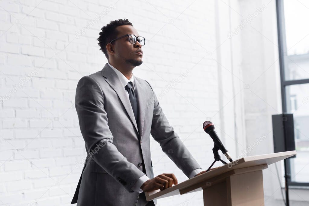 confident african american business speaker standing on podium with microphone in conference hall