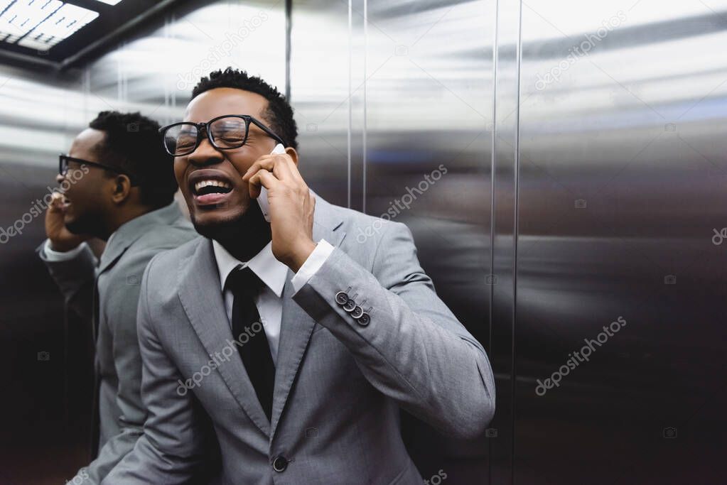 crying african american businessman talking on smartphone and suffering from panic attack in elevator