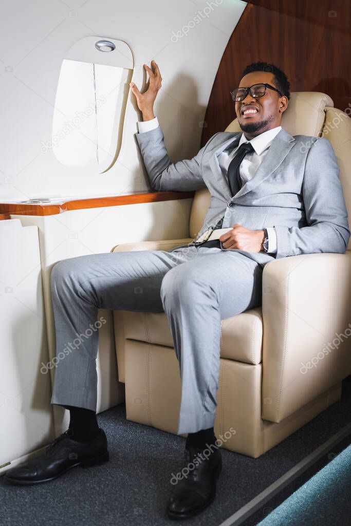 african american businessman holding safety belt and suffering from panic attack during flight on private plane