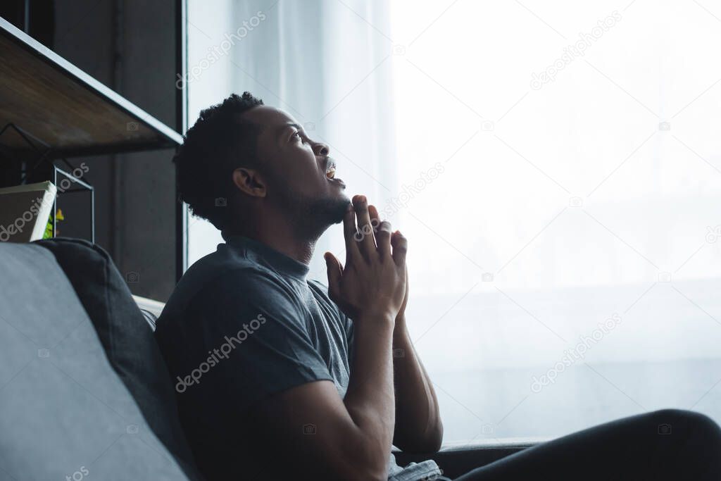 emotional african american man yelling with hands together on sofa at home