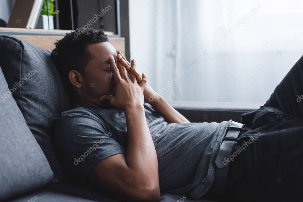 stressed african american man sitting on sofa at home