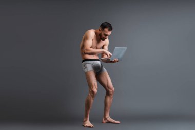 Üstsüz ve boxer şortlu adam gri dizüstü bilgisayar kullanıyor. 