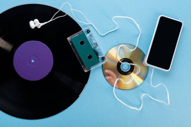 Vinil plağın üst görünümü, CD, kulaklık, ses bandı ve mavi üzerine boş ekran akıllı telefon, evrim konsepti 
