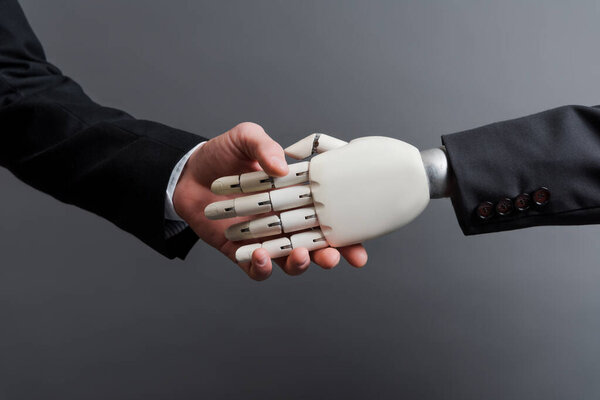 cropped view of businessman shaking hands with robot isolated on grey, evolution concept 