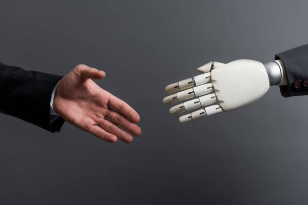 обрезанный взгляд бизнесмена жест рядом с роботом изолирован на сером, концепция эволюции
 