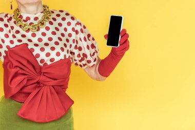 Sarı renkte izole edilmiş akıllı telefon tutan şık ve son sınıf kadınının görüntüsü.