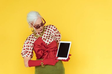 Sarı ekranda boş ekranlı dijital tablet tutan modaya uygun yaşlı bir kadın.