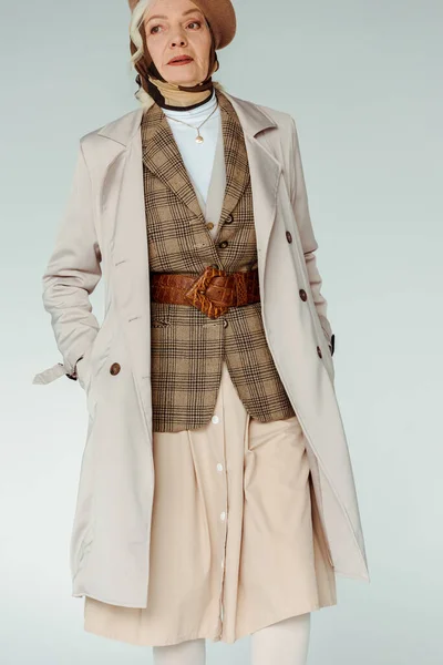 スタイリッシュな高齢者の女性で手でポケットにコート離れて隔離されたグレー — ストック写真