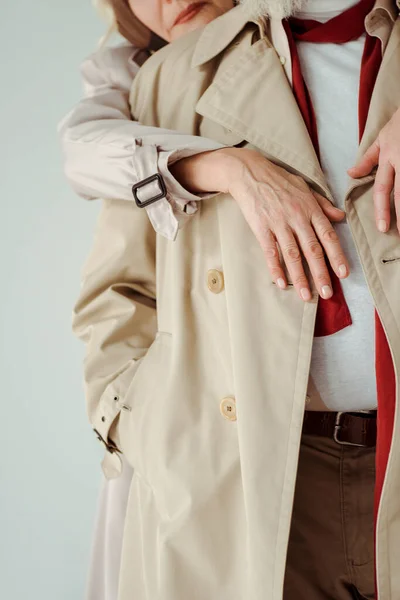 クロップドビューのシニア女性抱擁男でトレンチコート絶縁上グレー — ストック写真