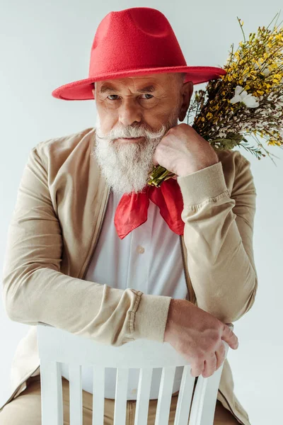 头戴红帽子 头戴红帽子的英俊老人 手持野花 凝视着坐在白色椅子上的相机 — 图库照片