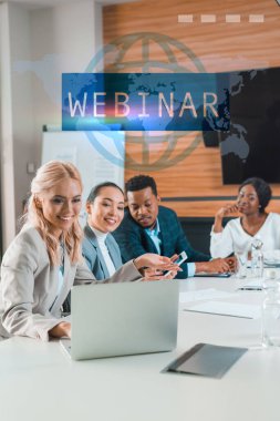 Gülümseyen çok kültürlü iş adamlarının seçici odağı konferans salonunda oturup dizüstü bilgisayara, webinar illüstrasyonuna bakıyorlar.