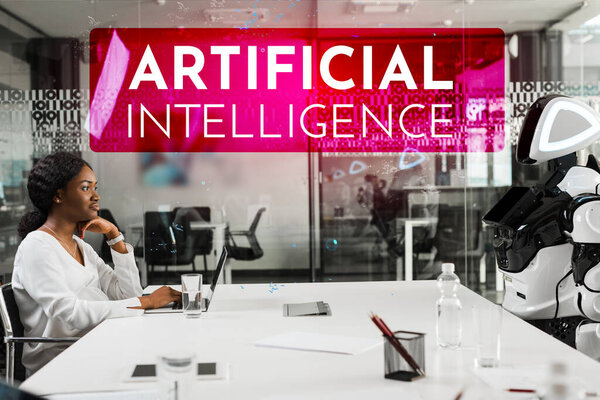 smiling african american businesswoman and robot sitting at desk in conference hall, Artificial Intelligence illustration