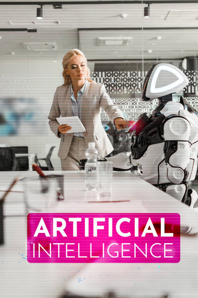 selective focus of attractive businesswoman operating robot while holding digital tablet, Artificial Intelligence illustration