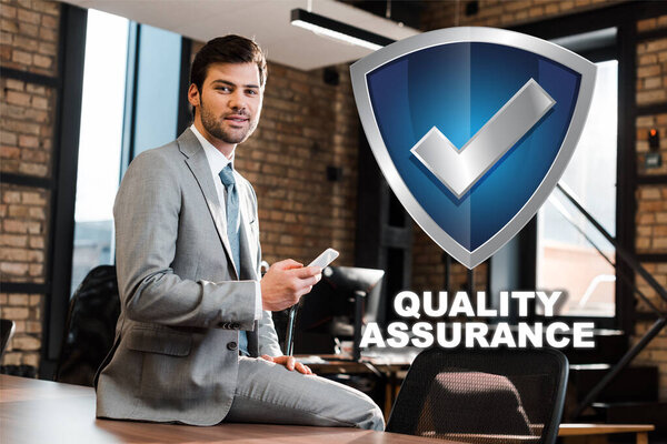 handsome, positive businessman sitting on office desk, holding smartphone and looking at camera, quality assurance illustration