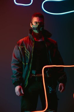 Koruyucu maskeli iki ırklı siber punk oyuncusu siyah ışığın yanında duruyor. 