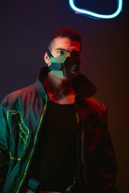 bi-racial cyberpunk player in protective mask near neon lighting on black  clipart