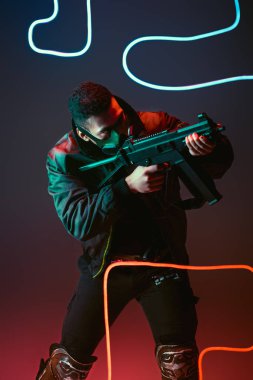 Koruyucu maskeli iki ırklı siber punk adam siyah ışığın yanına silah doğrultuyor. 