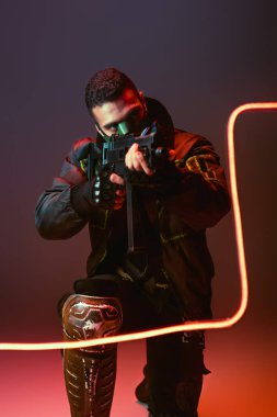 Maskeli iki ırklı siber punk adam siyah ışığın yanına silah doğrultuyor. 