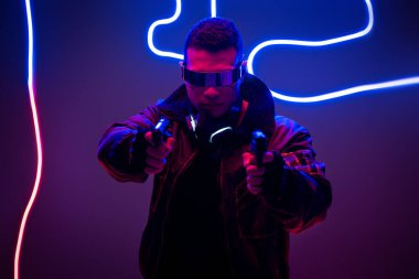 Fütürist gözlüklü karışık ırk siber punk oyuncusunun seçici odağı neon ışıklarının yanında silah tutuyor. 