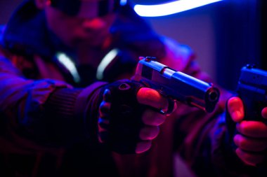 Neon ışıklandırması yakınında silah tutan çift ırklı siber punk oyuncusunun seçici odak noktası 