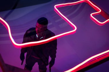 Kırmızı neon ışığın yanında silahlı, çift ırklı siber punk oyuncusunun tepeden görünüşü 