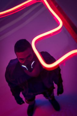 overhead view of mixed race cyberpunk player in mask near red neon lighting  clipart
