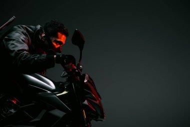 side view of dangerous bi-racial cyberpunk player in mask riding motorcycle on grey  clipart