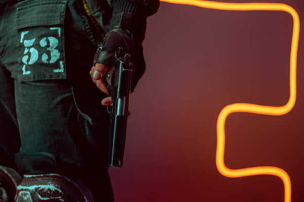 обрезанный вид опасного киберпанка с пистолетом на черном с неоновым освещением
 