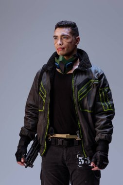 Yakışıklı ve silahlı çift ırklı siber punk oyuncusu gri üzerinde duruyor.  